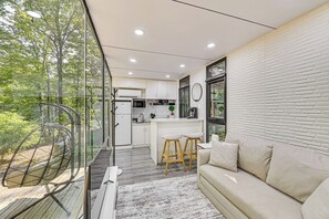 A modern kitchen with white cabinets, a dining area with stools, and a large window overlooking a forest.