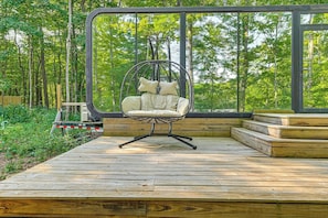 Una terraza de madera con una silla colgante y vista a un bosque.