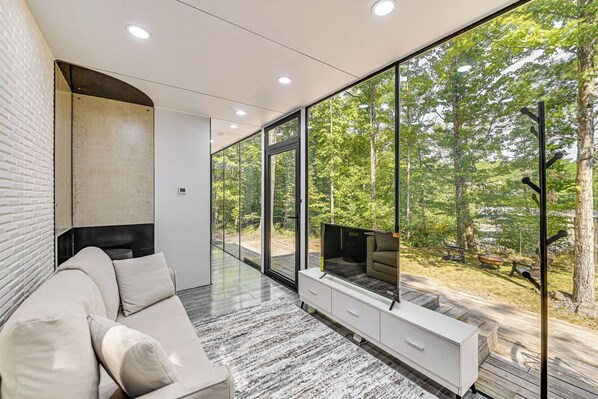 A modern interior with a sofa, a TV, and a large window overlooking a forest.