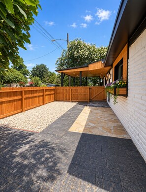 A covered outdoor area with a wooden fence, a stone pathway, and a building with windows. - Heights Gem Chef's Kitchen 5 Min to Downtown (Houston)