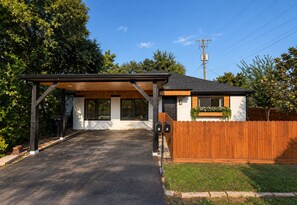 A modern house with a covered driveway, a fenced backyard, and a utility pole. - Heights Gem Chef's Kitchen 5 Min to Downtown (Houston)