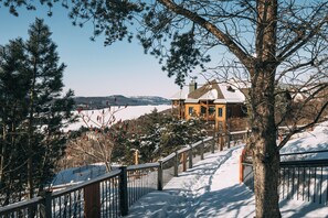 A snow-covered staircase leading to a house with a view of a lake and mountains. - Equinox Condo | Ski-in/Ski-out  | Stunning Lake & Mountain View | Pool Access (Mont-Tremblant)