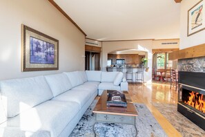 A modern living room with a sectional sofa, a coffee table, and a fireplace. - Equinox Condo | Ski-in/Ski-out  | Stunning Lake & Mountain View | Pool Access (Mont-Tremblant)