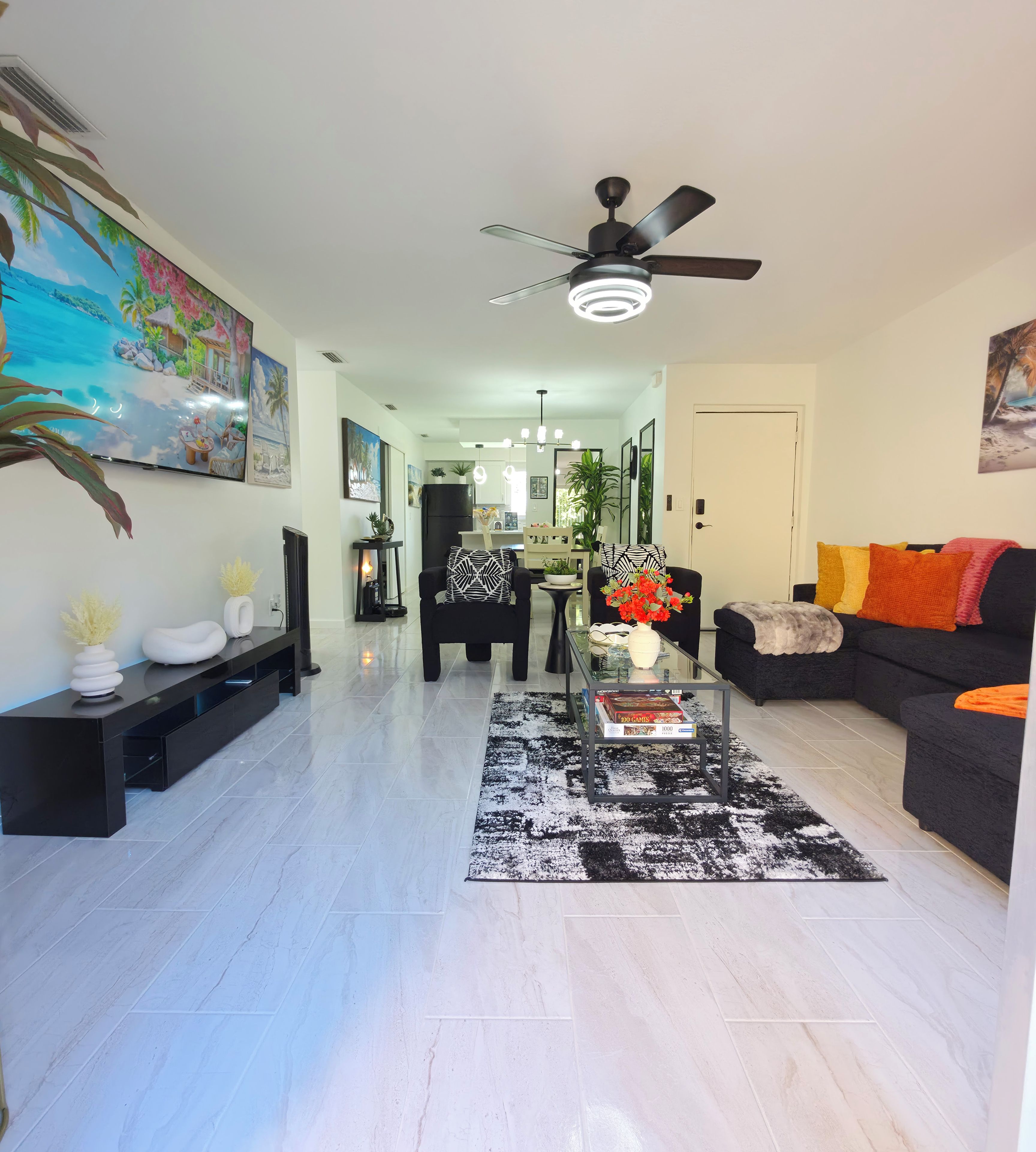 Un salon moderne avec une table basse en verre, un canapé noir et un ventilateur de plafond.