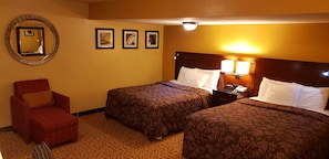 A hotel room with two beds, a red armchair, a round mirror, and three framed pictures on the wall. - Regal inn  (Coffeyville)