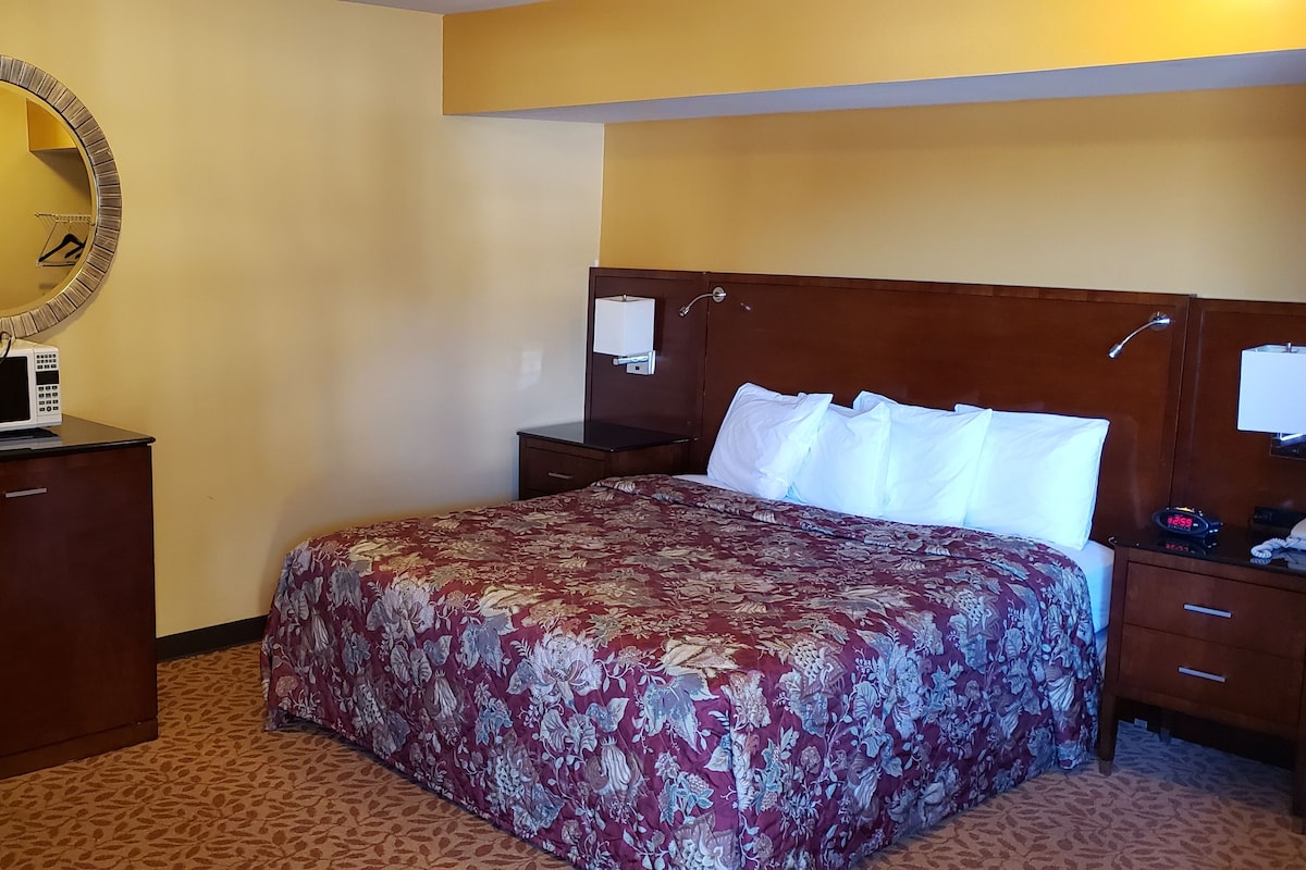 A hotel room with a bed, bedside tables, a desk with a lamp, a mirror, and a clock.