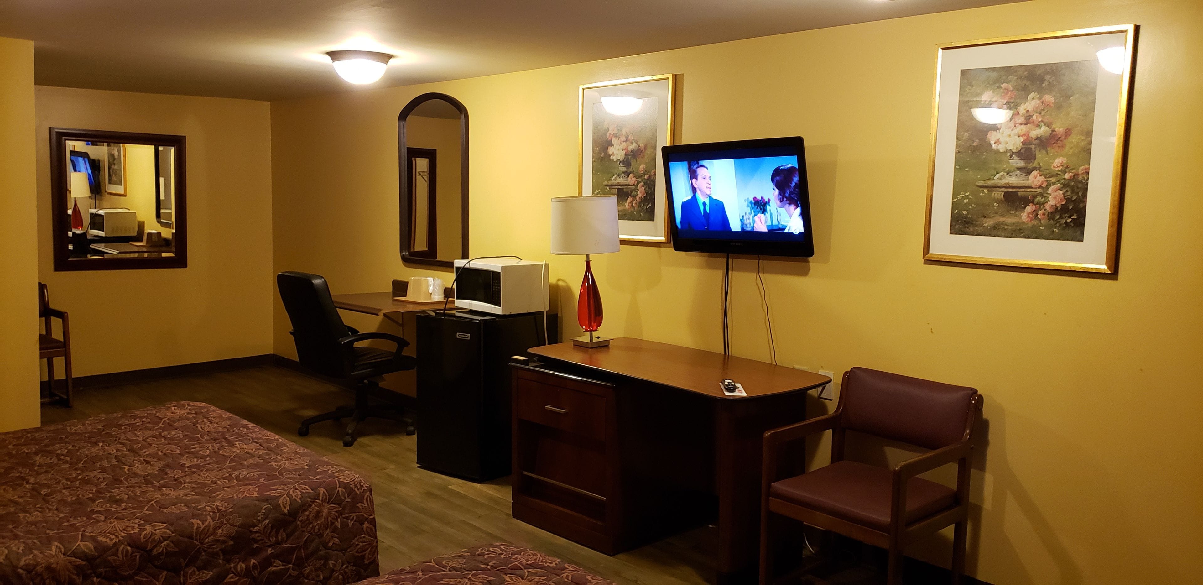 A hotel room with a bed, a desk with a computer, a television, and a chair.