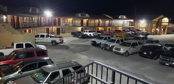 Un estacionamiento con varios vehículos, un edificio con balcón y un cartel de hotel.