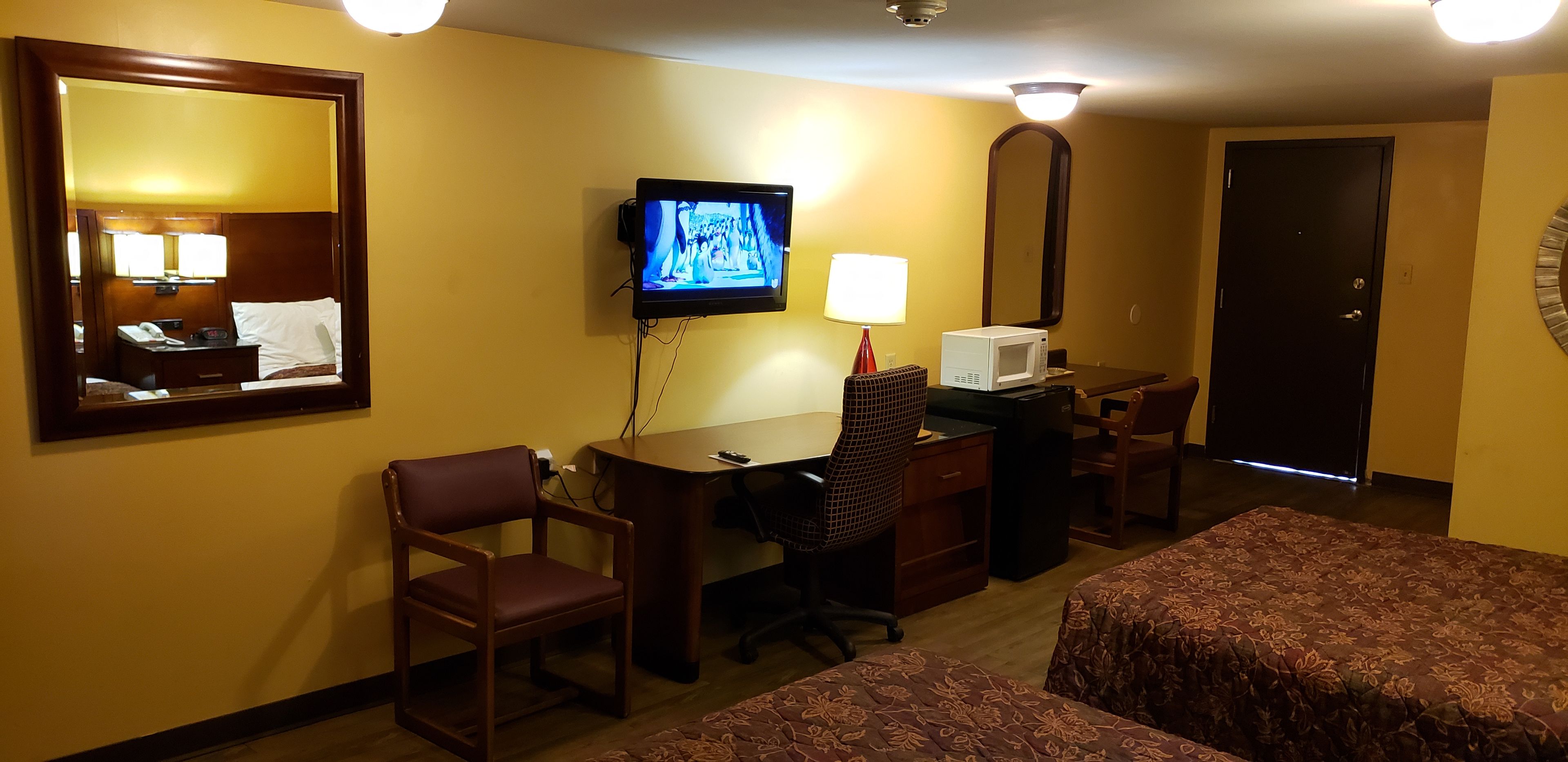 A hotel room with a desk, chair, television, lamp, microwave, and two beds.