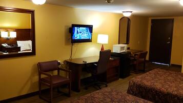 A hotel room with a desk, chair, television, lamp, microwave, and two beds.