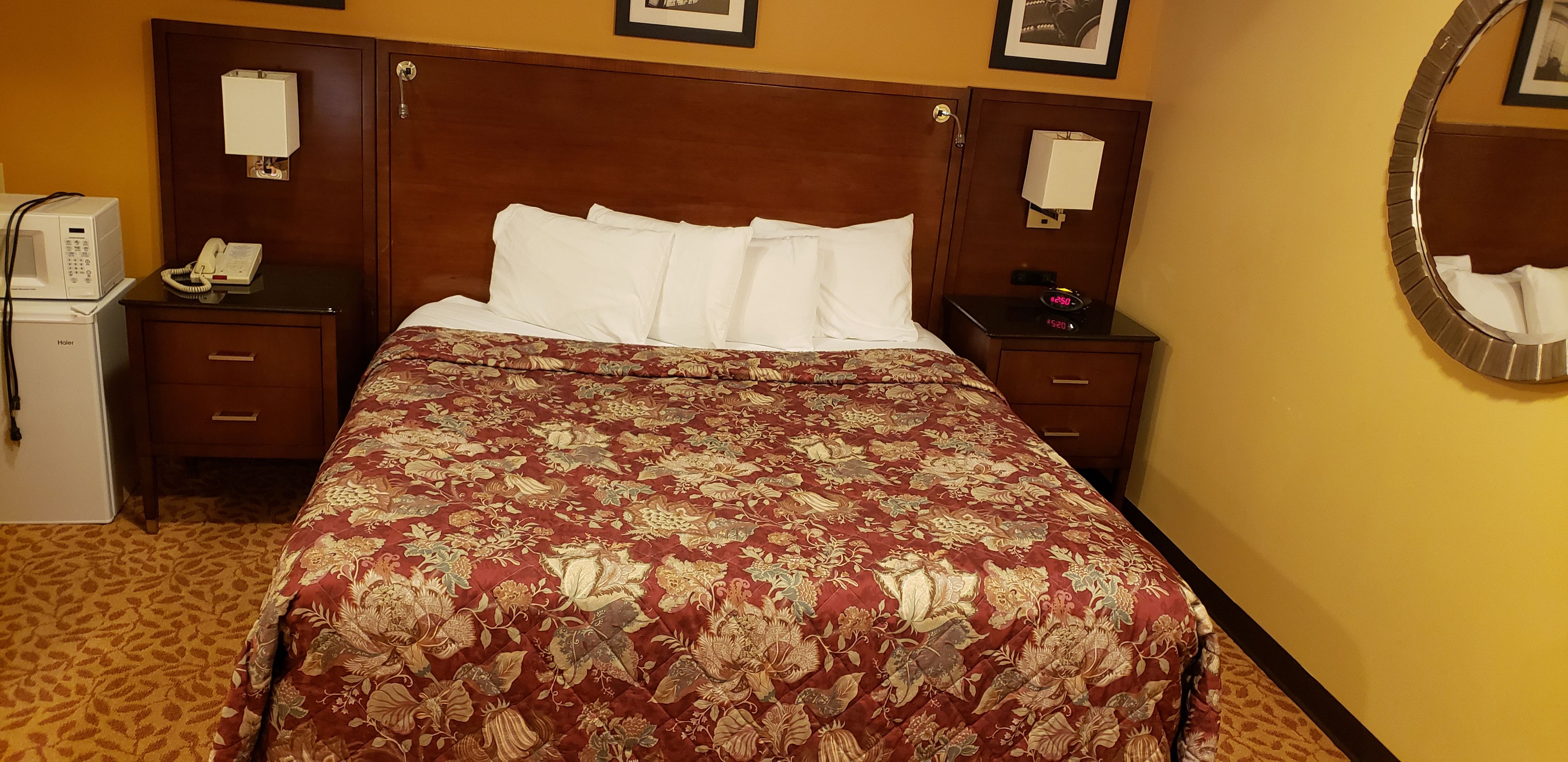 A hotel room with a large bed, two bedside tables, a built-in heater, a telephone, and a mirror on the wall.