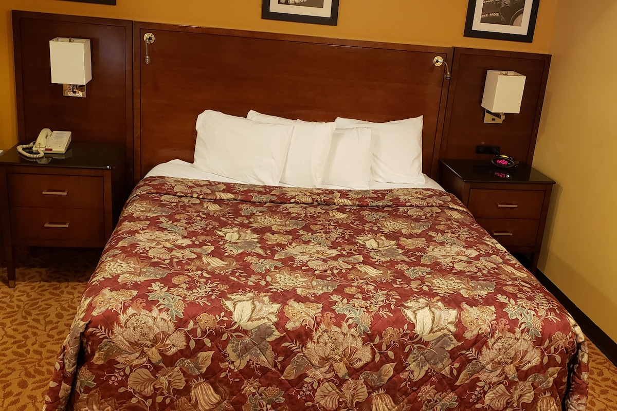 A hotel room with a large bed, two bedside tables, a built-in heater, a telephone, and a mirror on the wall.