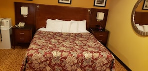 A hotel room with a large bed, two bedside tables, a built-in heater, a telephone, and a mirror on the wall. - Regal inn  (Coffeyville)