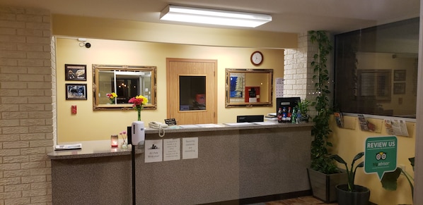 A reception desk with a clock, framed pictures, and a 'Review Us' sign. - Regal inn  (Coffeyville)