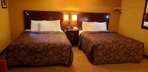 A hotel room with two beds, a nightstand, a lamp, and a mirror. - Regal inn  (Coffeyville)