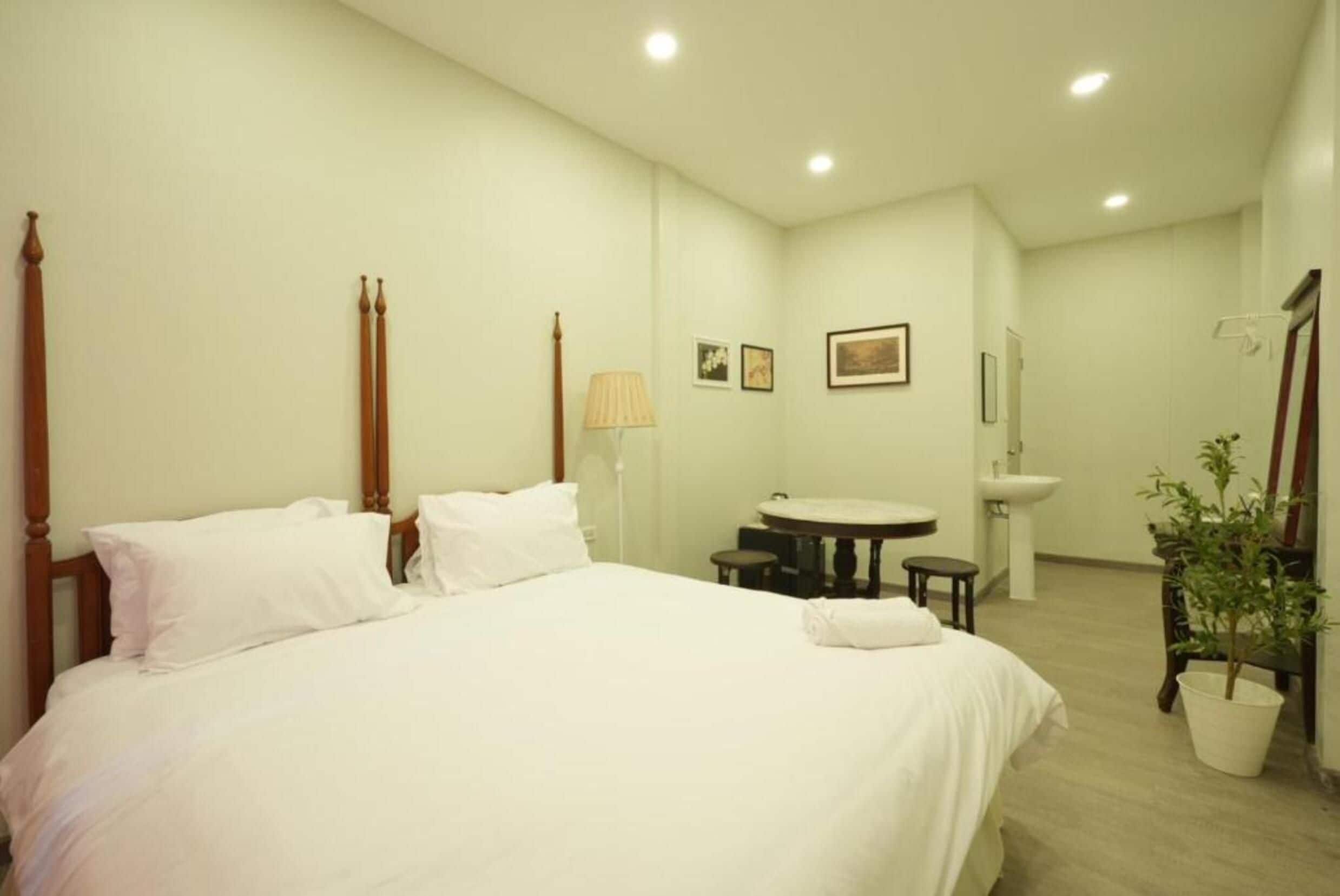 Ein Hotelzimmer mit einem großen Bett, einem Nachttisch, einem kleinen runden Tisch, einem Sessel, einer Lampe, einem Waschbecken und einem Spiegel.