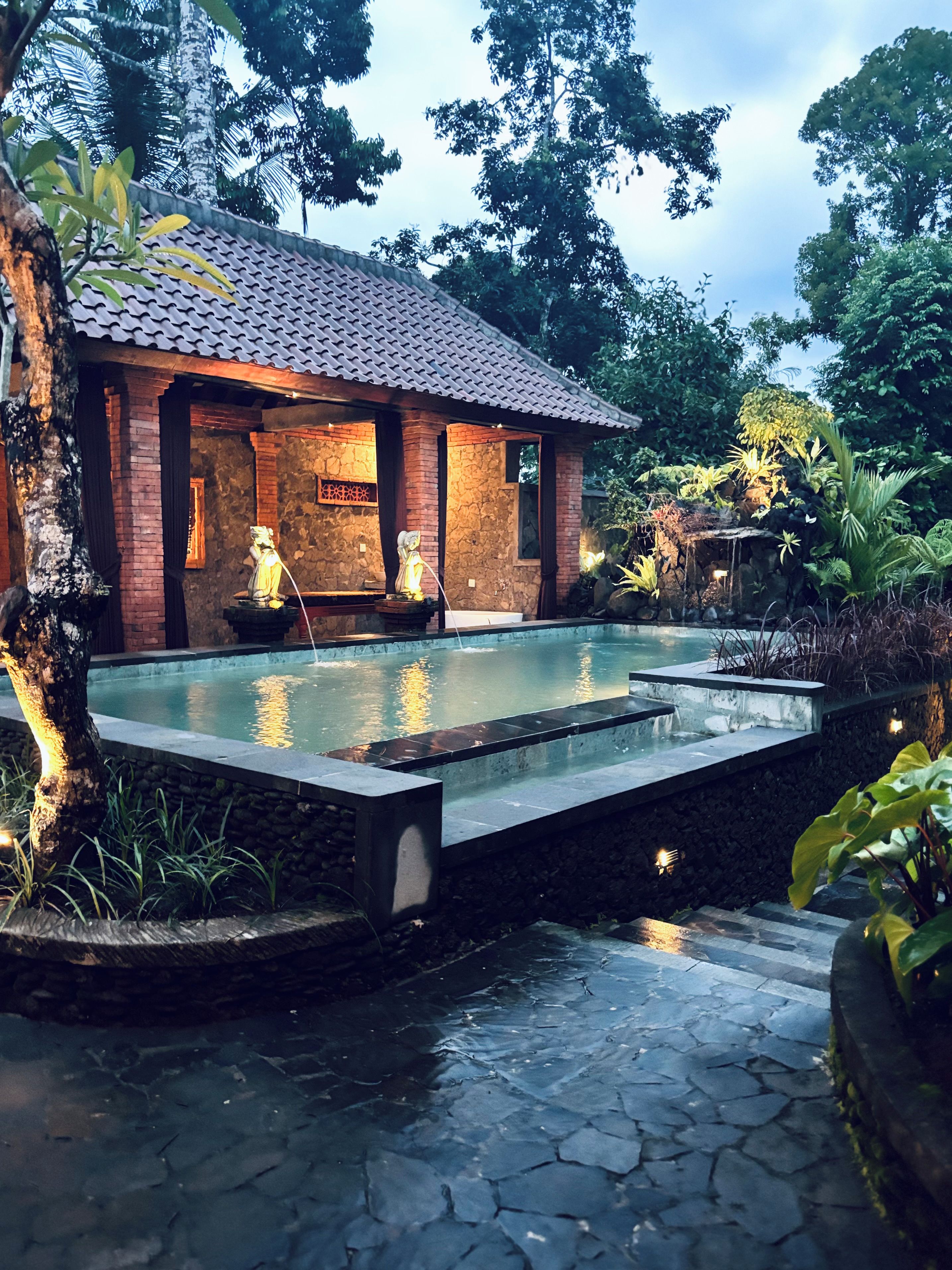 Un edificio con techo de tejas, piscina y estatuas.