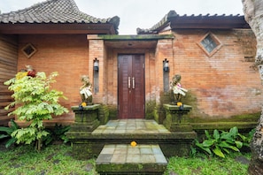 A traditional brick building with a tiled roof, a wooden door, and two stone statues on either side of the entrance.