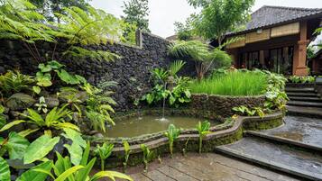A stone wall with a water feature, lush greenery, and a traditional building with a tiled roof.