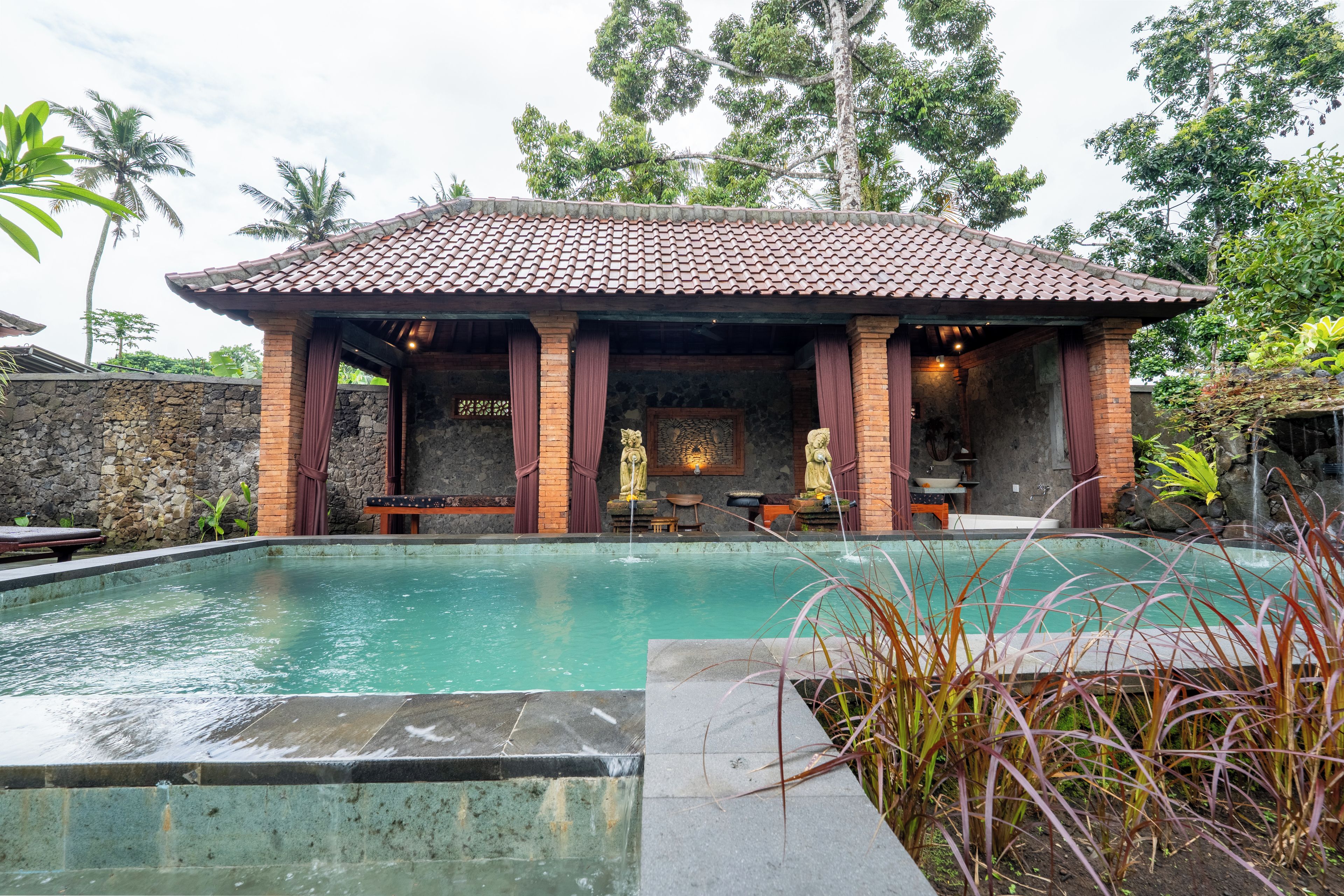 A pool area with a tiled roof structure, stone walls, and a statue.