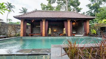 A pool area with a tiled roof structure, stone walls, and a statue.