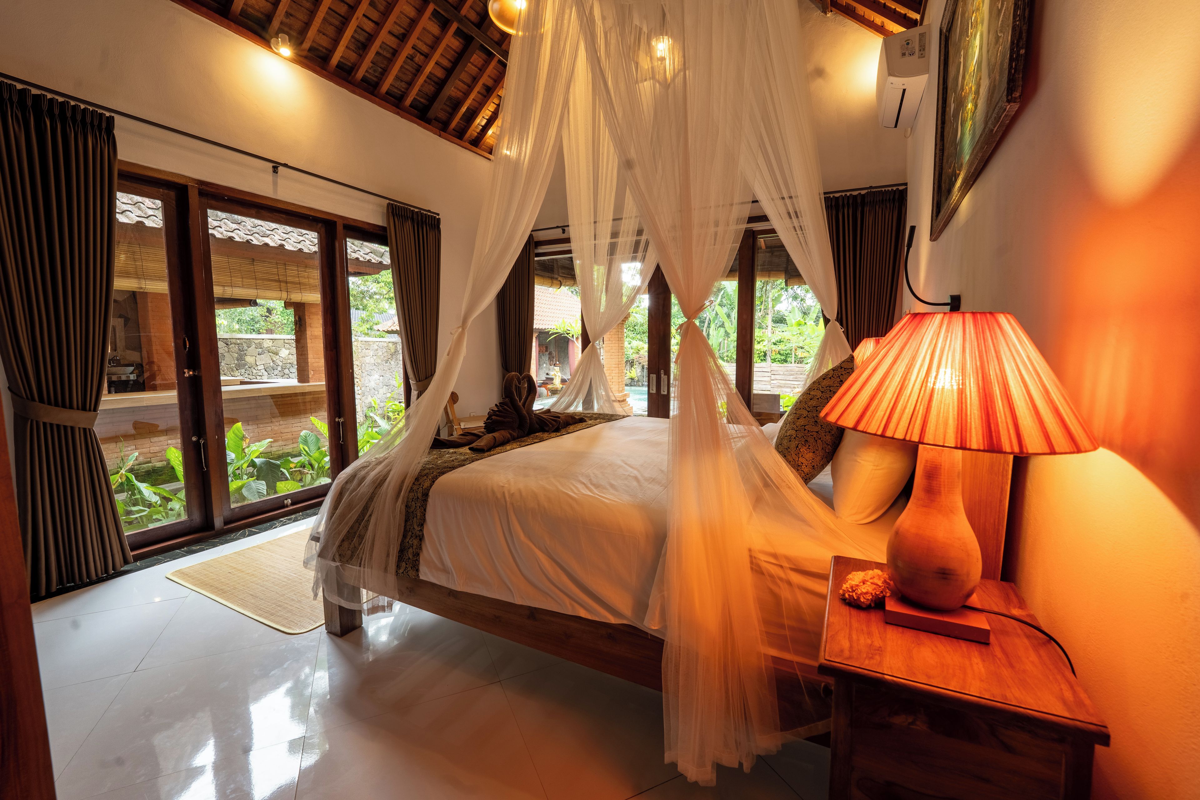 Un dormitorio con cama con dosel, lámpara de noche y vistas al jardín.