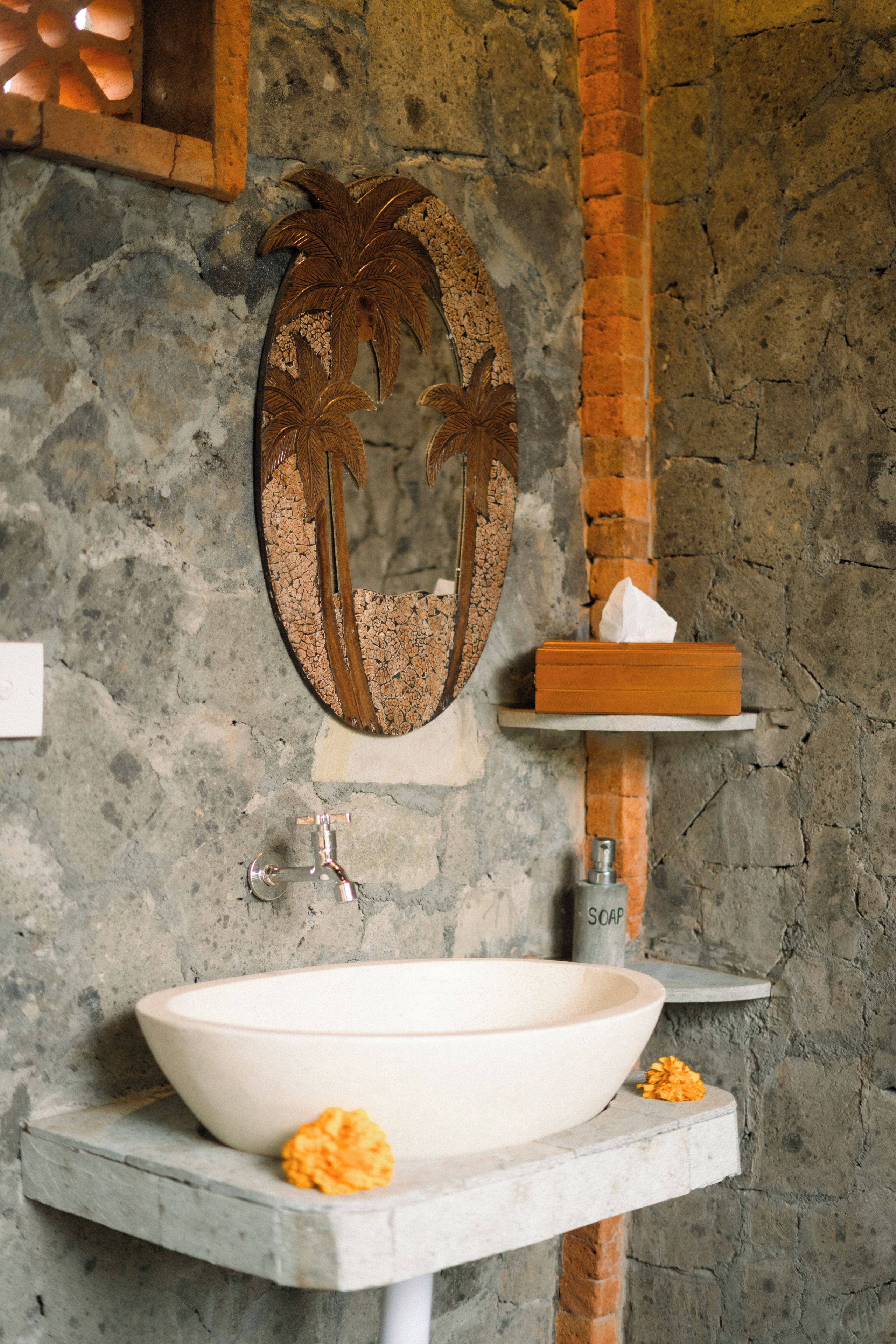 A bathroom with a white sink, a mirror with a palm tree design, and a soap dispenser.