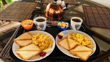 Una bandeja de desayuno con huevos revueltos, tostadas, café y una tetera sobre una mesa de vidrio.