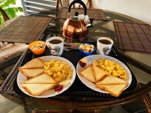 Un plateau de petit-déjeuner avec des œufs brouillés, des toasts, du café et une théière, posé sur une table en verre.