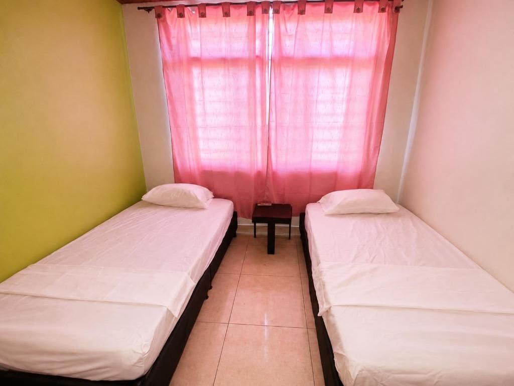 Ein Zimmer mit zwei Einzelbetten, einem kleinen Tisch und einem Vorhang.
