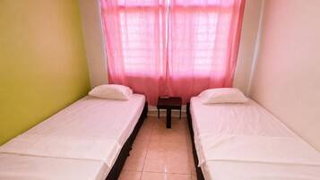 Ein Zimmer mit zwei Einzelbetten, einem kleinen Tisch und einem Vorhang.