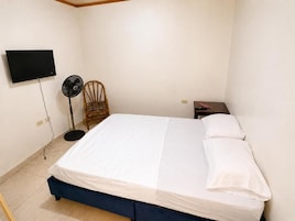Un dormitorio con cama, una silla, un televisor y una mesita de noche.