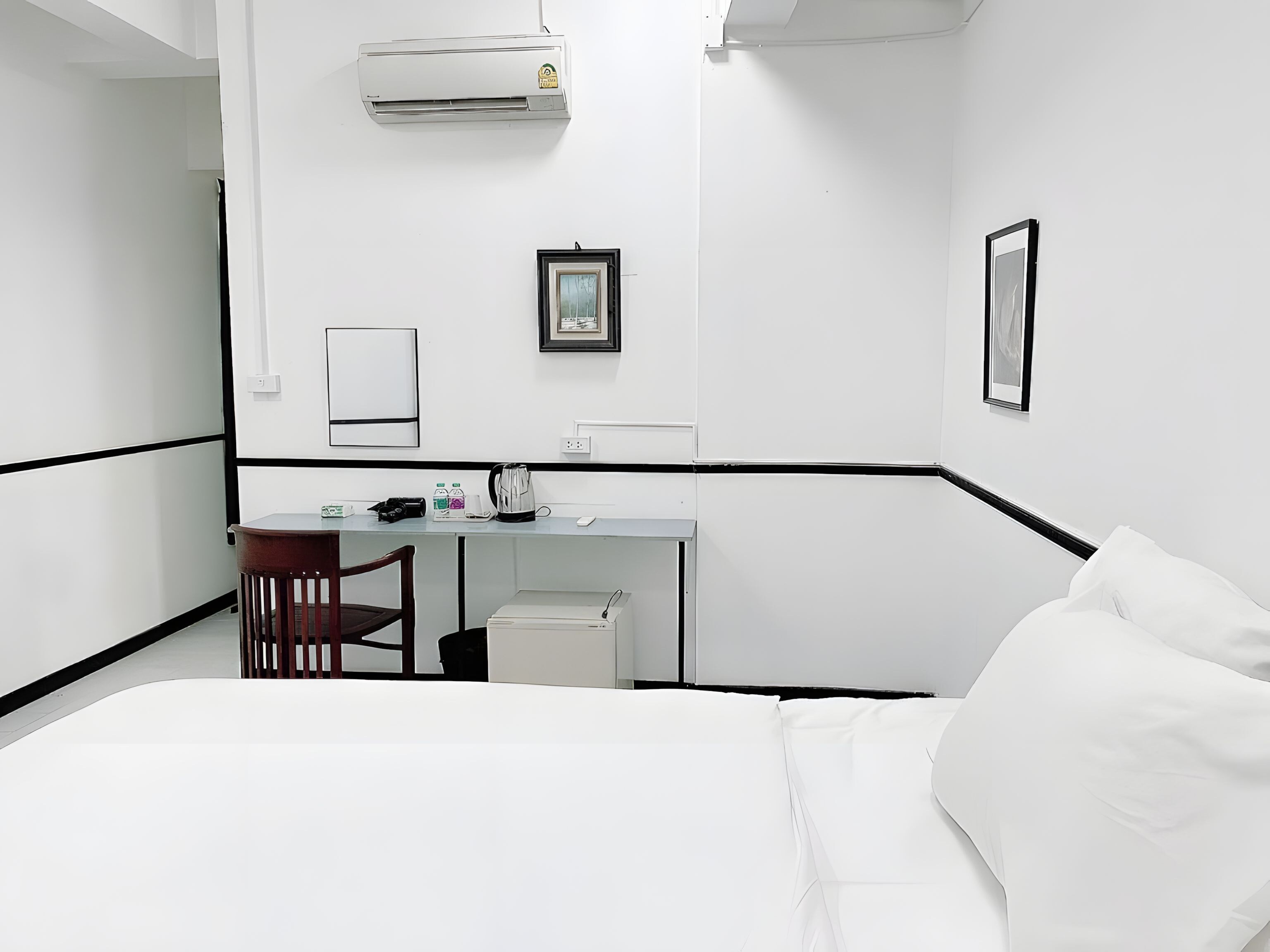 A hotel room with a bed, desk, chair, and an air conditioning unit.