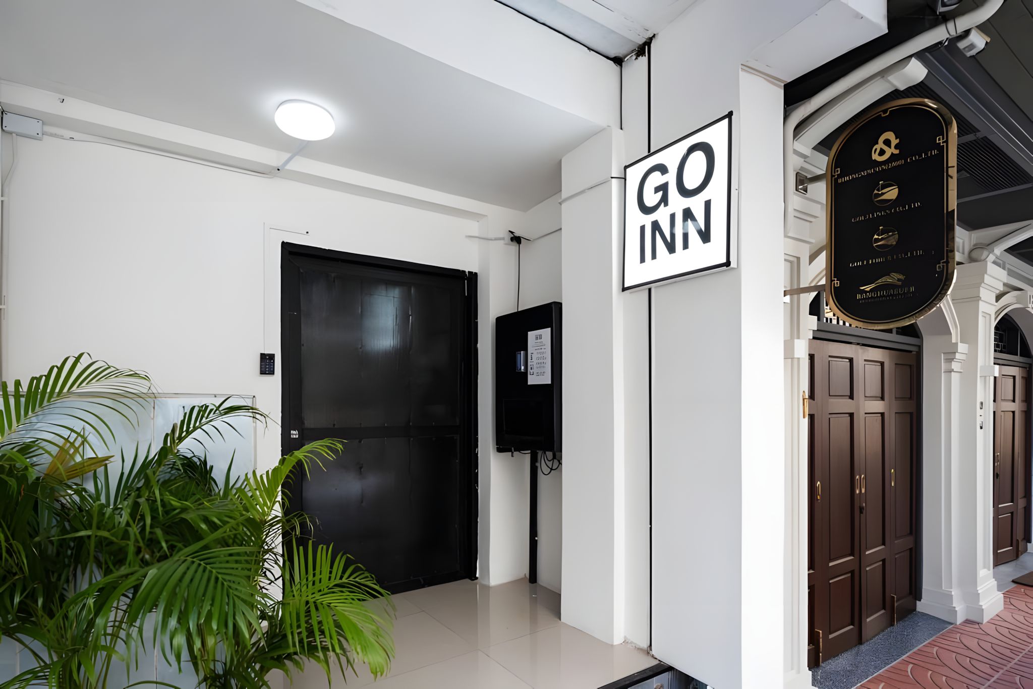 A hotel entrance with a closed black door, a Go Inn sign, a television mounted on the wall, and a potted plant.