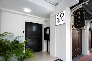 Entrada d'hotel amb una porta negra tancada, un rètol de Go Inn, un televisor fixat a la paret i una planta en test.