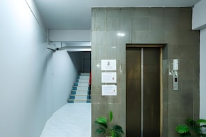 A modern elevator with a metallic finish, a staircase with blue and yellow steps, and two potted plants. - B room Hualumphong (Bangkok)