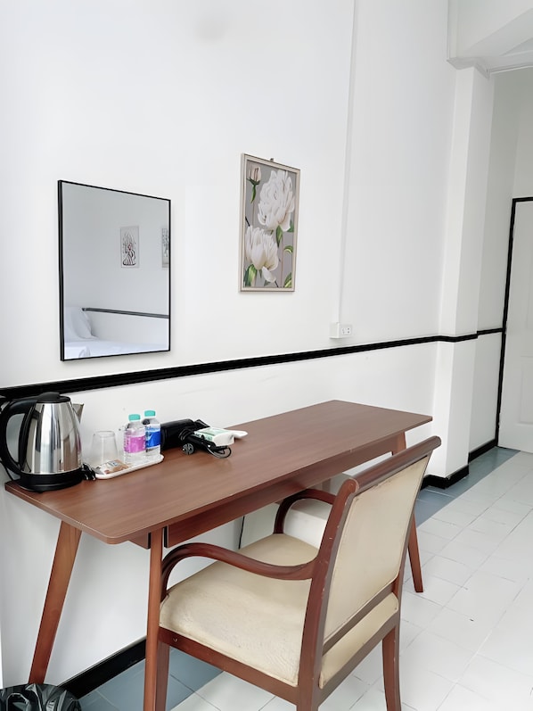 A hotel room with a wooden desk, a chair, a kettle, and a framed floral artwork on the wall. - B room Hualumphong (Bangkok)