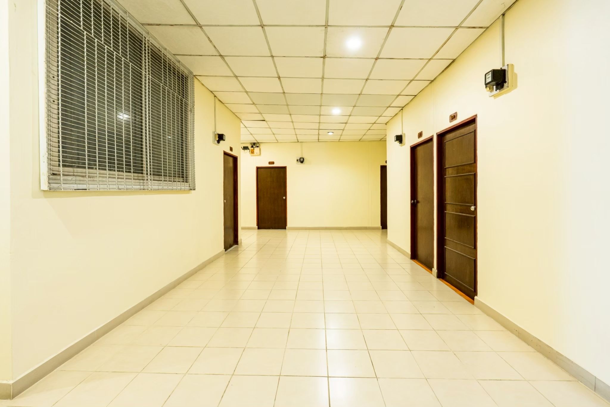A corridor with tiled flooring, a window with blinds, and doors on both sides.