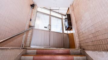 Eine Treppe führt zu einer Tür, an der sich ein Metallgeländer und ein Schild mit der Aufschrift 'Aufzug' befinden.