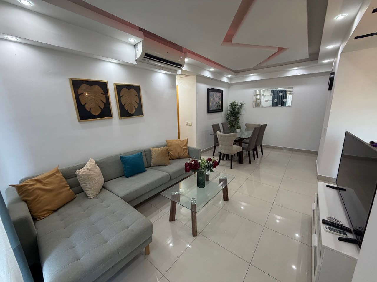 Una sala moderna con un sofá gris, una mesa de centro de vidrio y un mueble para televisión.