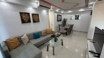 Una sala moderna con un sofá gris, una mesa de centro de vidrio y un mueble para televisión.