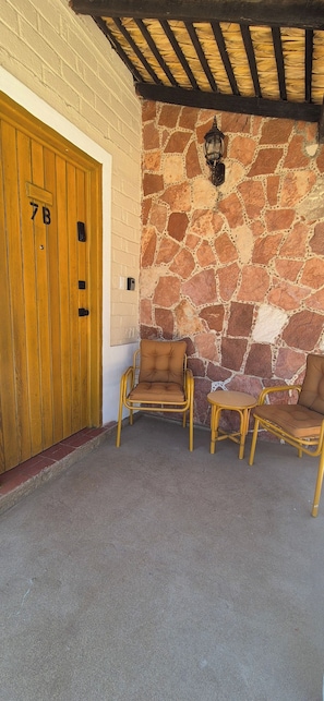 A stone wall with a wooden door marked '7B' and a bench area with two chairs and a small table. - Sandy Shores 7B (La Paz)