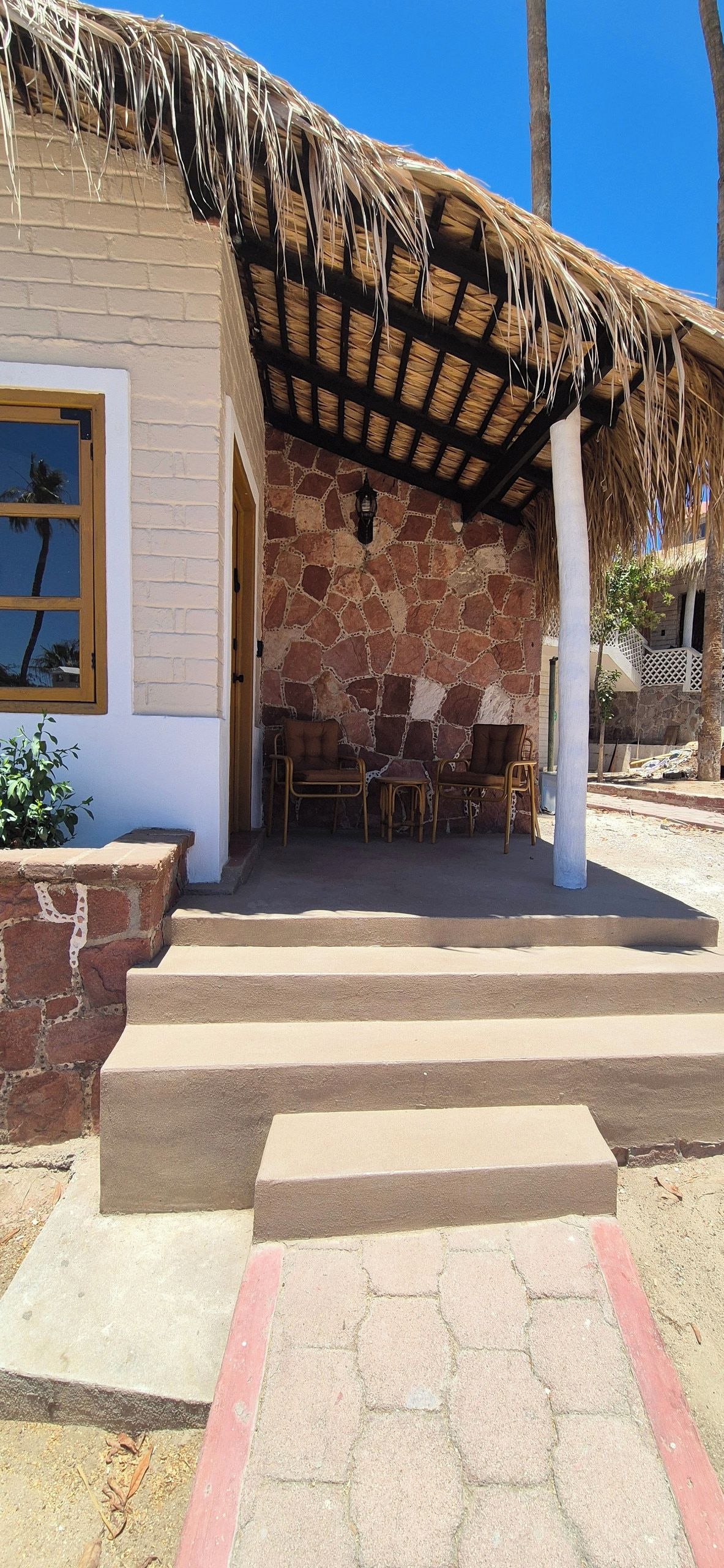 A building with a stone facade, a thatched roof, and a set of outdoor steps leading to a seating area with chairs.
