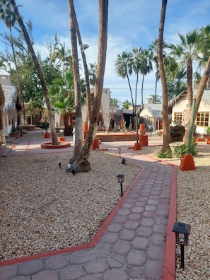 A paved pathway lined with palm trees and a thatched-roof building.