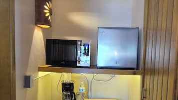 Habitación de hotel compacta con kitchenette, televisión de pantalla plana, lámpara de pared y puerta de madera.