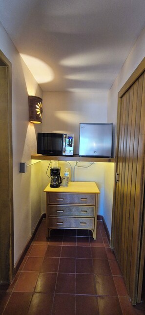Quarto de hotel compacto com cozinha compacta, televisão de tela plana, luminária fixada na parede e porta de madeira.