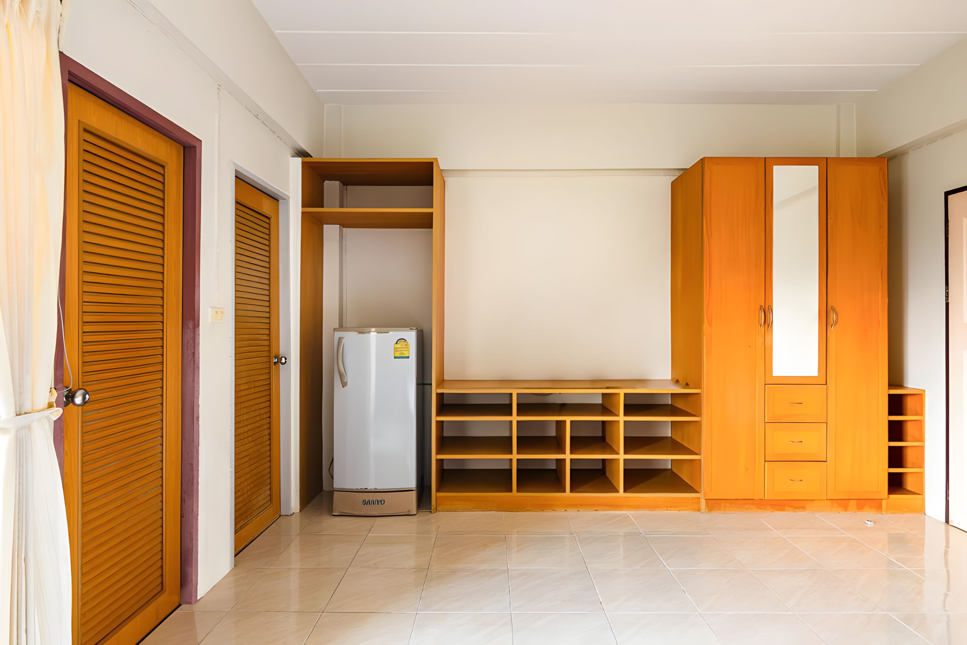 A room with a wardrobe, a built-in shelf unit, and a refrigerator.