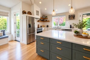 Une cuisine moderne dotée d’un grand îlot central, d’appareils électroménagers en acier inoxydable et offrant une vue sur la verdure environnante.