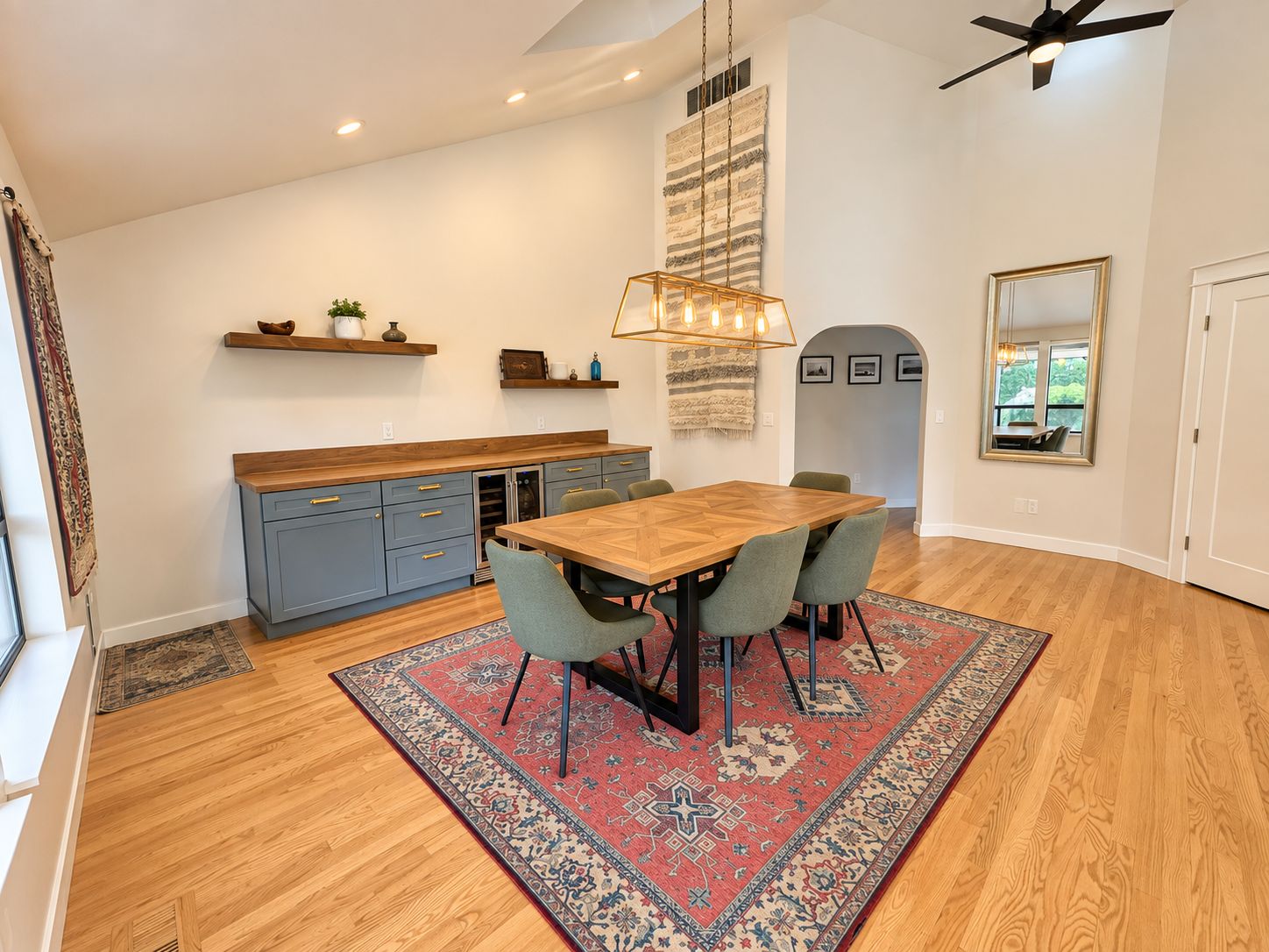 A modern kitchen with a wooden table and chairs, a ceiling fan, and a rug.