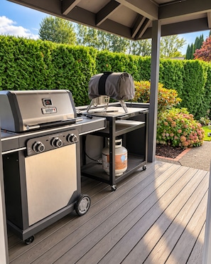 Un barbecue Weber à usage commercial, doté d’une table d’appoint et d’une bouteille de gaz, installé sur une terrasse en bois.